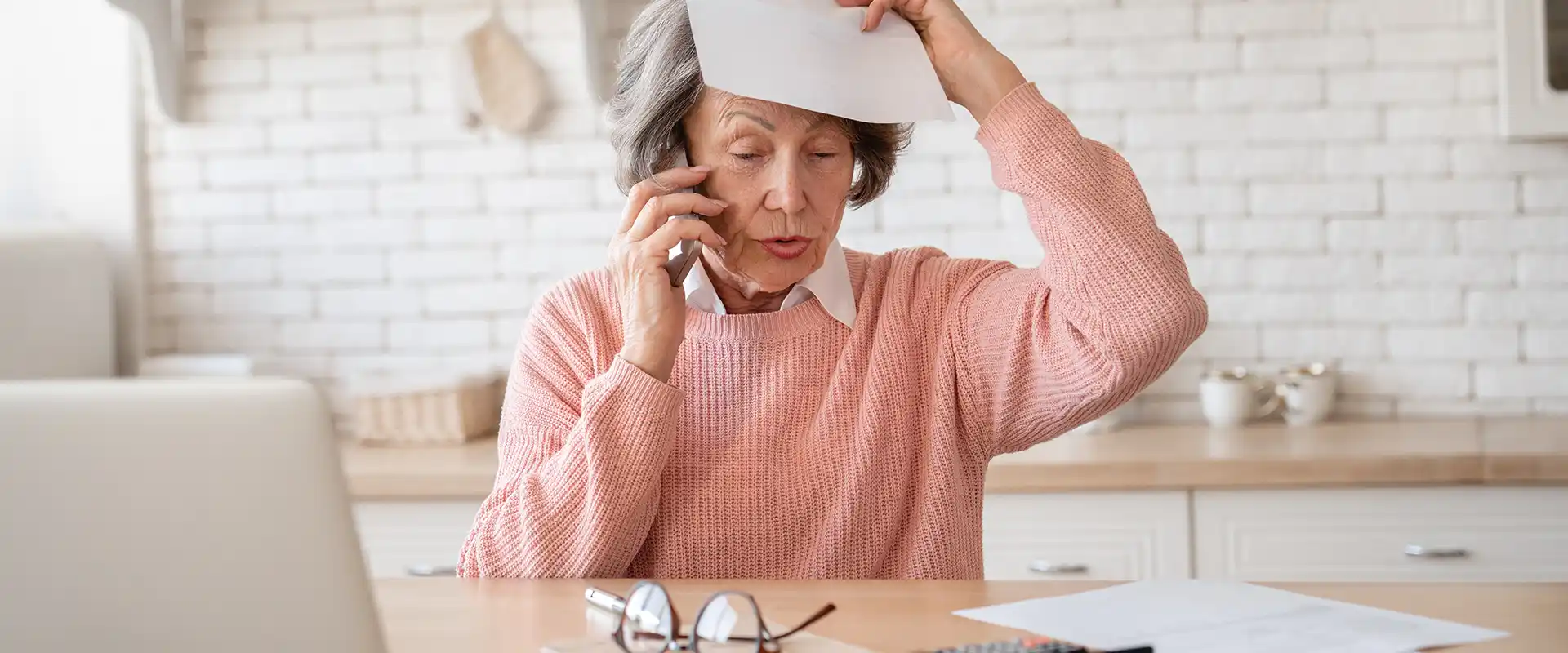 Pflegegrad Widerspruch - Ältere Seniorin am Schreibtisch schlägt sich ein Papier über den Kopf beim telefonieren - Amor Pflegedienst