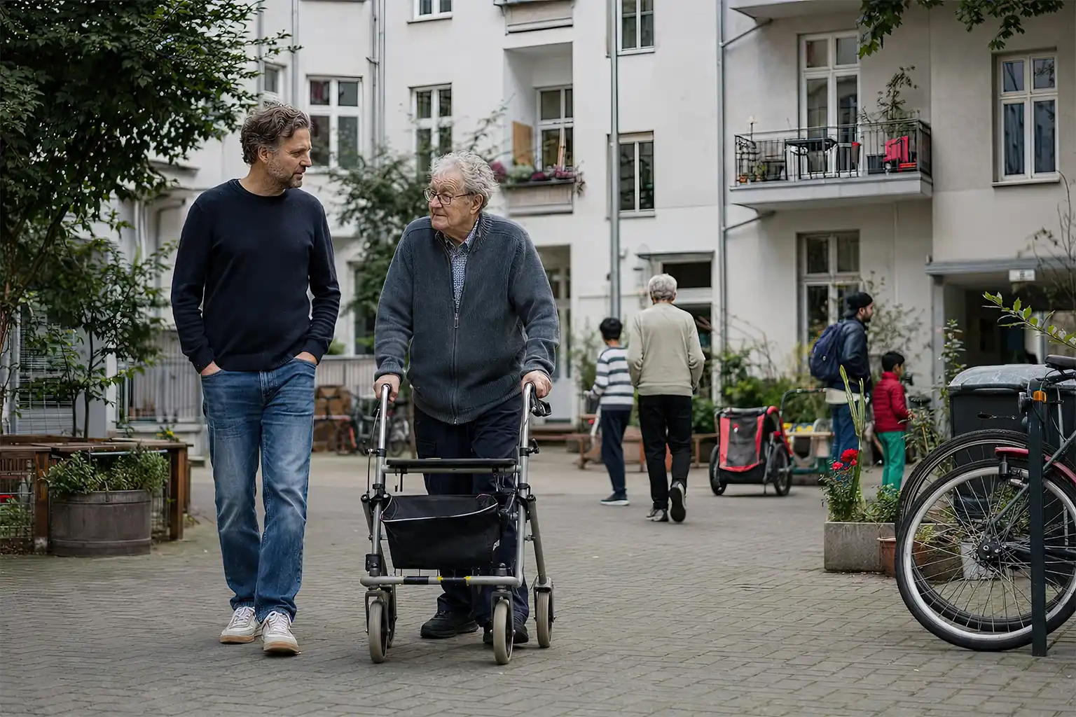 Älterer Mann mit Rollator und sein Sohn im Gespräch in einem Berliner Innenhof.